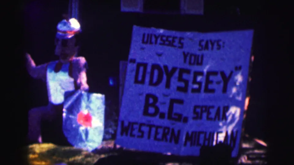 1963 Bowling Green University home-movie frame showing a costumed figure and a hand-painted sign referencing Ulysses, Odyssey, B.G., and Western Michigan.