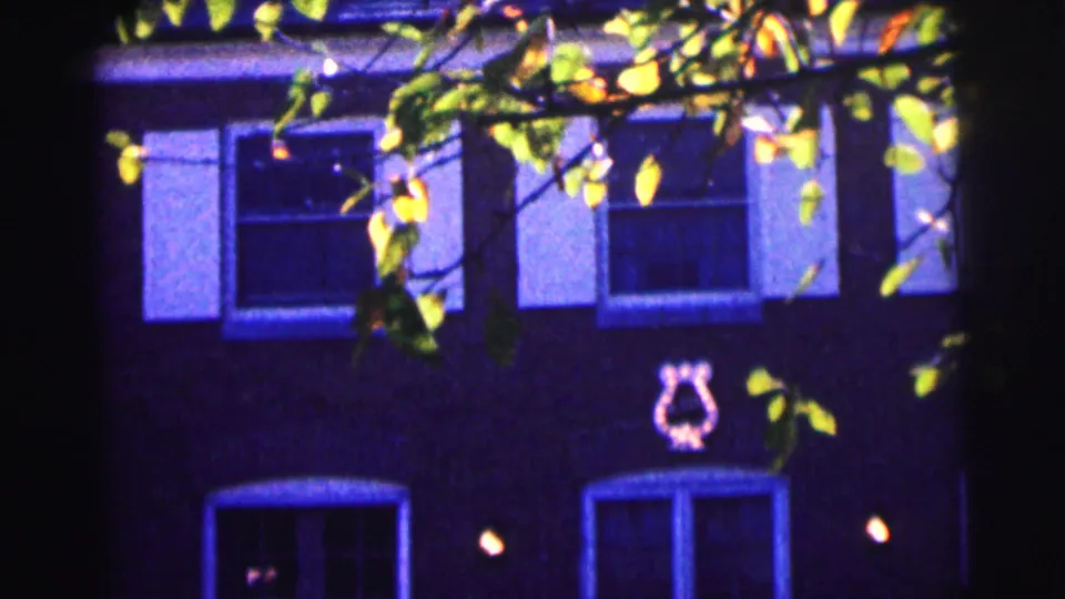 Bowling Green University exterior with windows, tree branches, and a lyre-like wall symbol in blue-tinted 8mm footage.