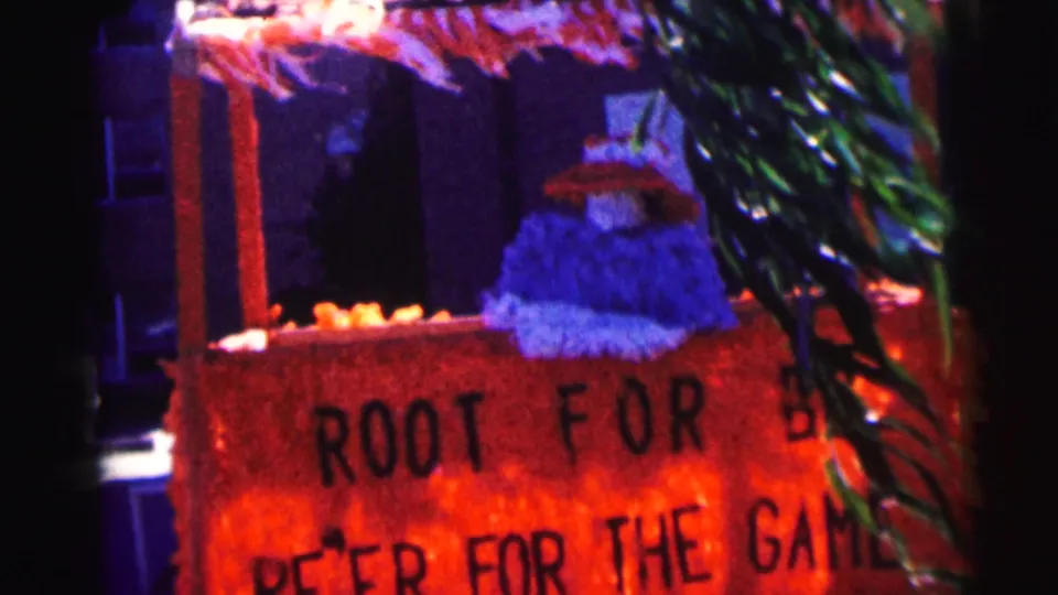 Bowling Green University home-movie frame showing a red foreground sign with partial game-support text and campus building behind.