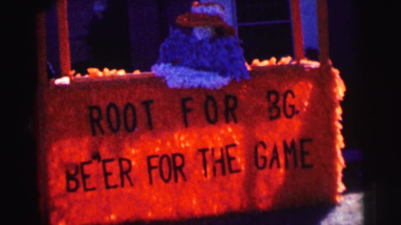 Painted orange sign reading ROOT FOR BG and BE'ER FOR THE GAME on a decorated house front.