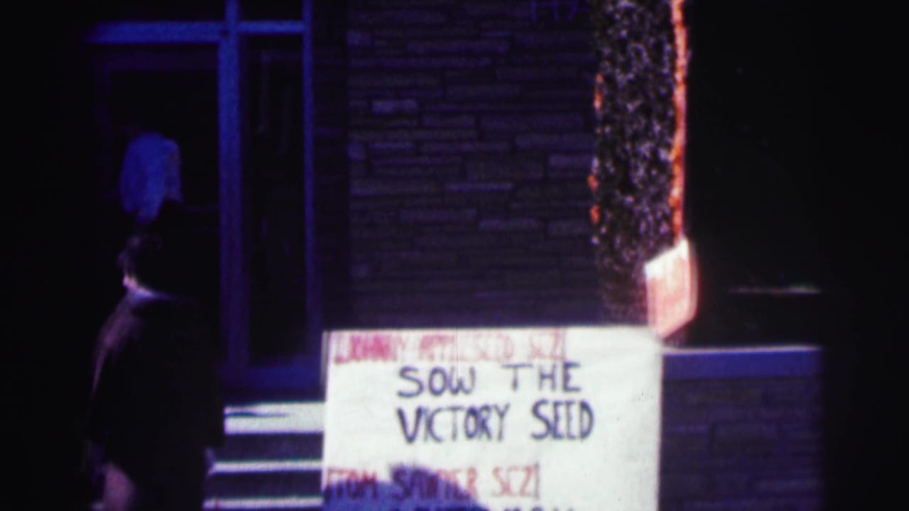 1963 Bowling Green University nighttime exterior with a handmade sign by a brick doorway and a passerby in dark clothing.