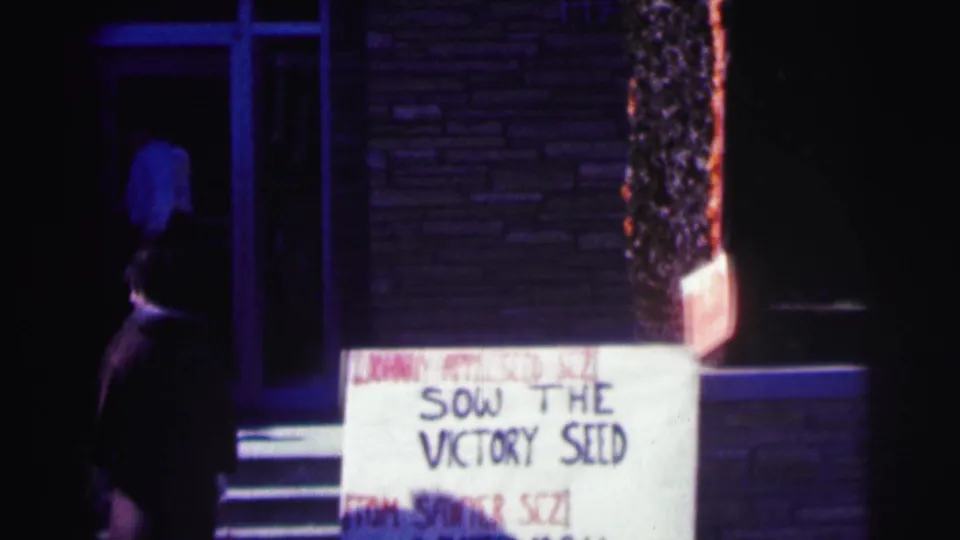 1963 Bowling Green University nighttime exterior with a handmade sign by a brick doorway and a passerby in dark clothing.