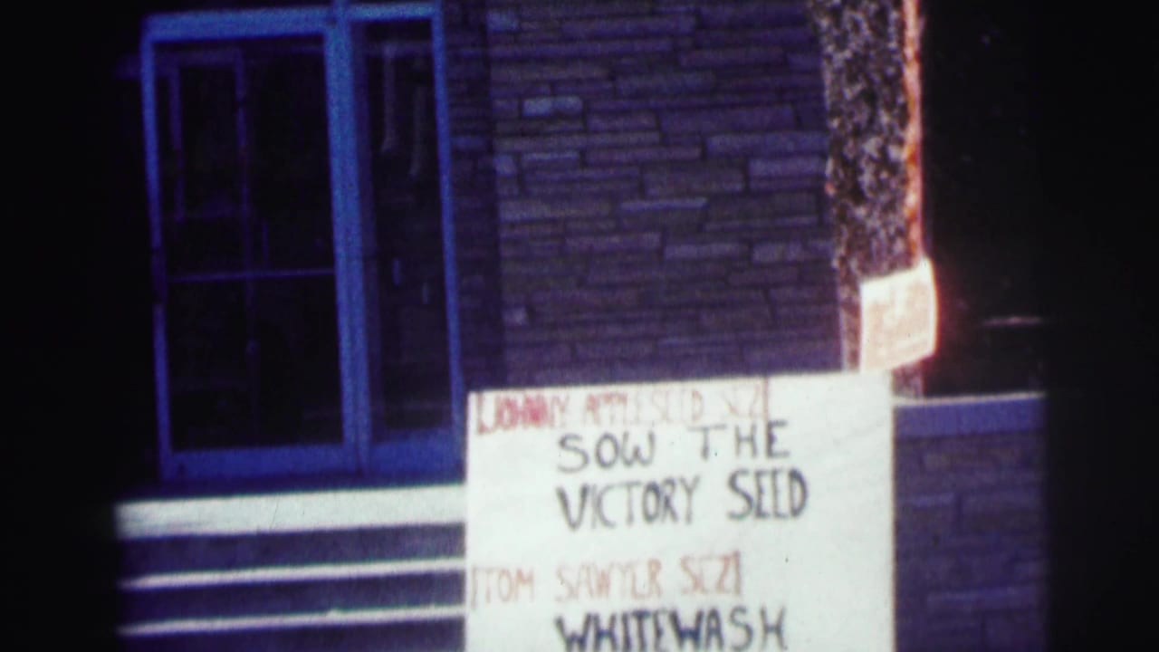 Night exterior at Bowling Green University showing a sign reading Sow the Victory Seed near a brick entrance and steps.