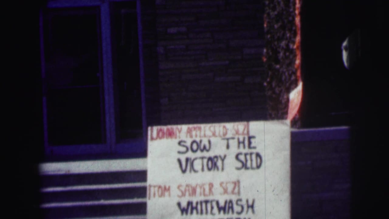 1963 Bowling Green University home-movie frame showing a handmade sign with folk-character phrases beside a building exterior.