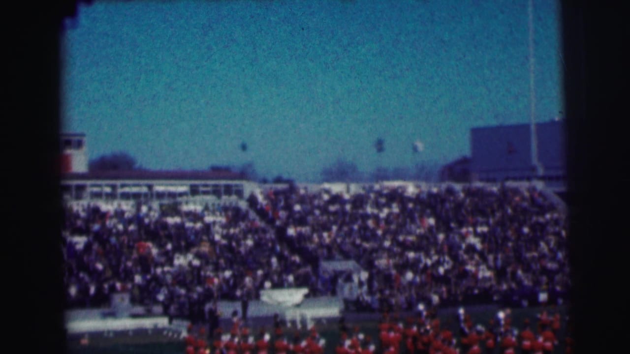 Wide stadium view with crowded bleachers and a band on the field.