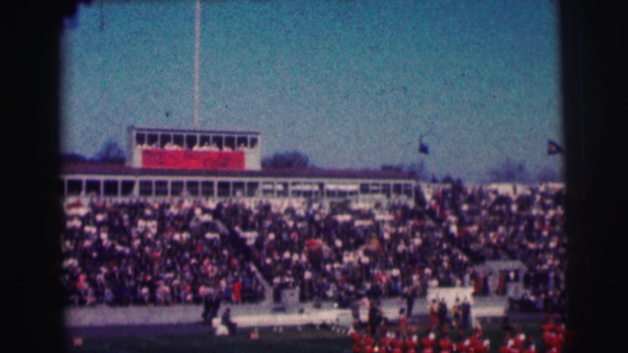 Crowded Bowling Green University stadium scene with press box, flags, and red band uniforms visible in 1963 home-movie footage.