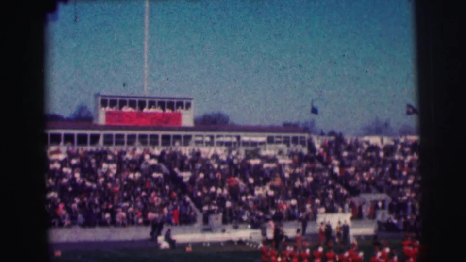 Crowded Bowling Green University stadium scene with press box, flags, and red band uniforms visible in 1963 home-movie footage.
