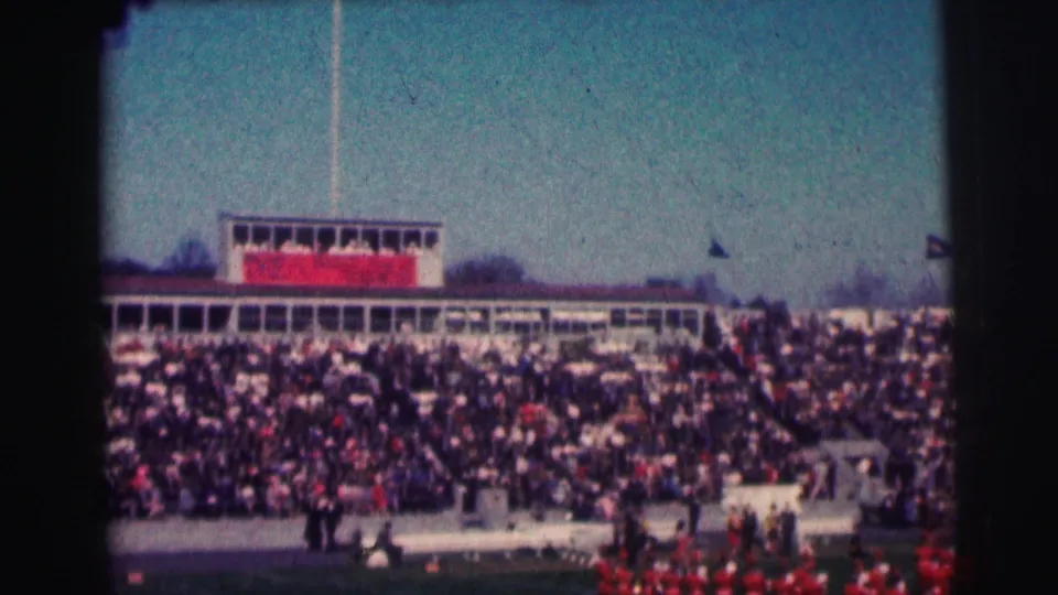 1963 stadium view at Bowling Green University showing dense spectators, a press box, and red marching band members near the field.