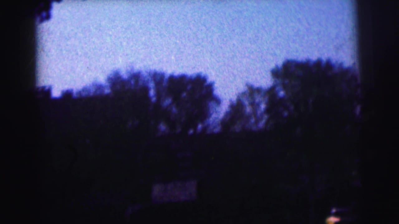 Dark stadium view with trees, sky, and a distant sign or scoreboard.