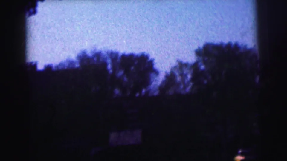 Dim 8mm frame from the Bowling Green University clip showing trees, sky, and a shadowed stadium area after the band view.
