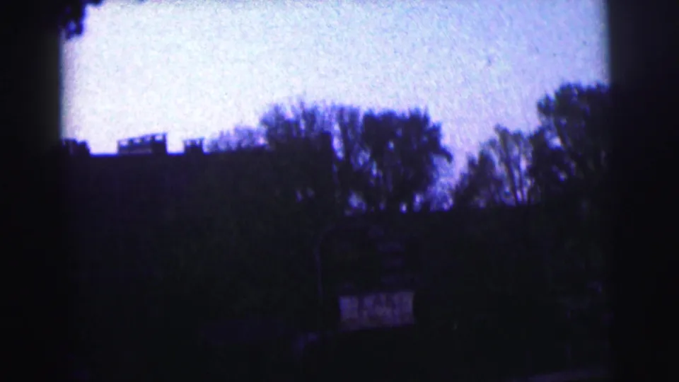Underexposed 1963 campus-stadium frame with silhouetted trees, sky, and a small sign-like shape in the lower area.
