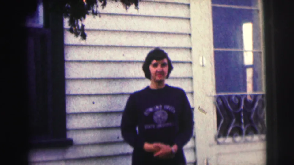 Woman in a dark lettered sweatshirt stands outside a light-sided building, consistent with 1963 Bowling Green University home-movie footage.