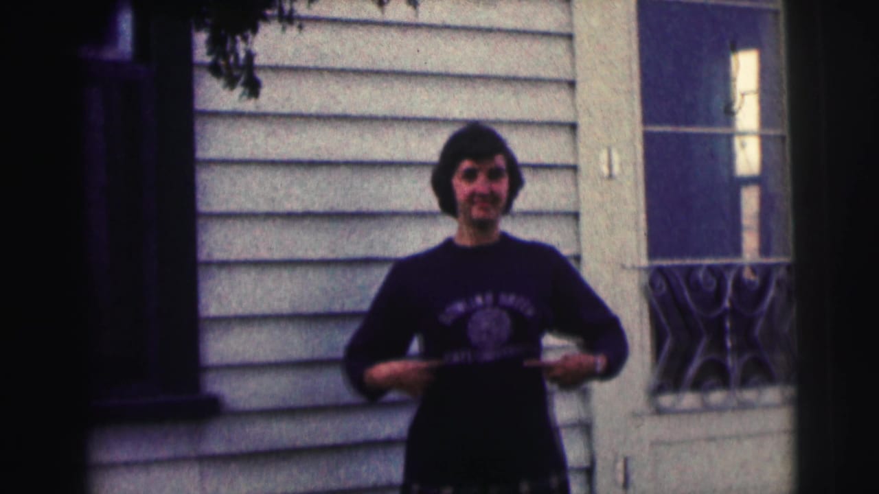 In 1963 home-movie footage, a woman in a Bowling Green State University sweatshirt stands outside a light-sided house.