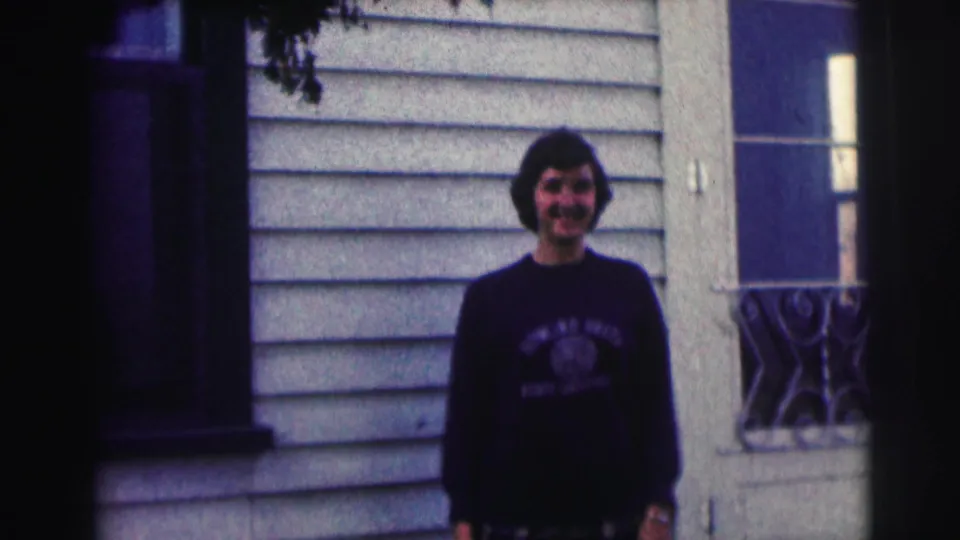 A woman in a Bowling Green State University sweatshirt stands in front of house siding, framed by windows and railing.