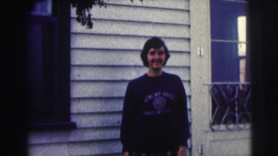 Smiling young man remains posed in front of a light-sided exterior with a window, wearing a Bowling Green State University sweatshirt.