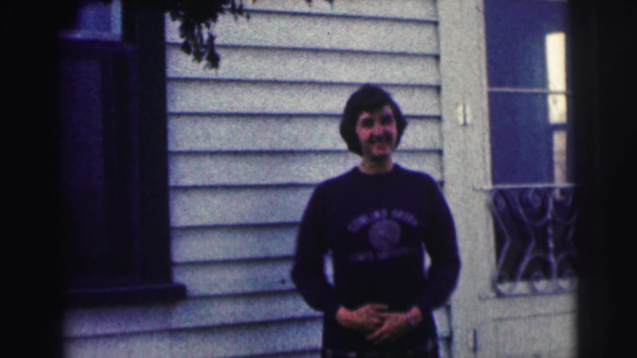 Young man smiles outside the house with his hands lowered near his waist.