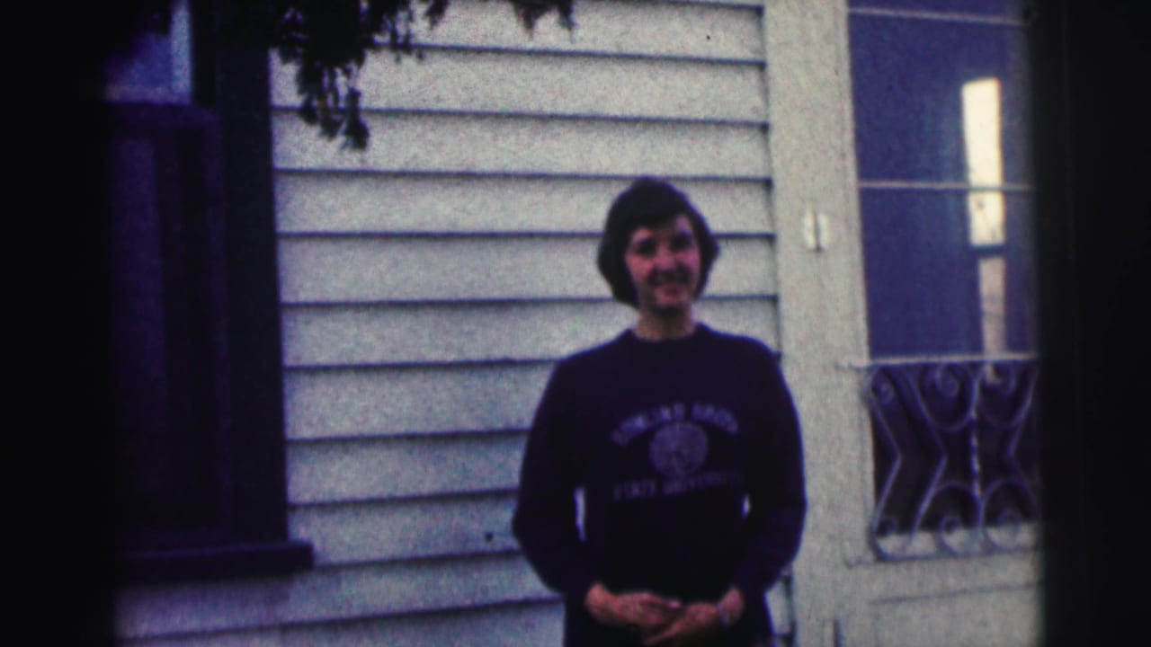 Young woman in a Bowling Green State University sweatshirt smiles outside a light-sided house in 1963 home-movie footage.