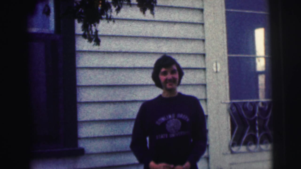 Young woman stands smiling with hands clasped in front of siding and a glass door.