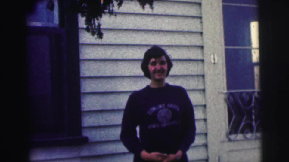 Young woman smiles at the camera in a dark Bowling Green State University sweatshirt outside a light-sided house.