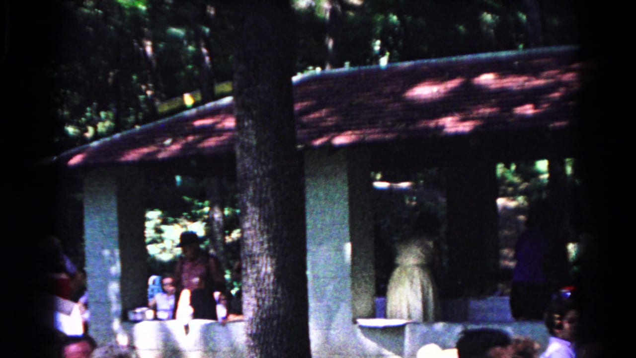 People stand by the pavilion counter while trees shade the roof.