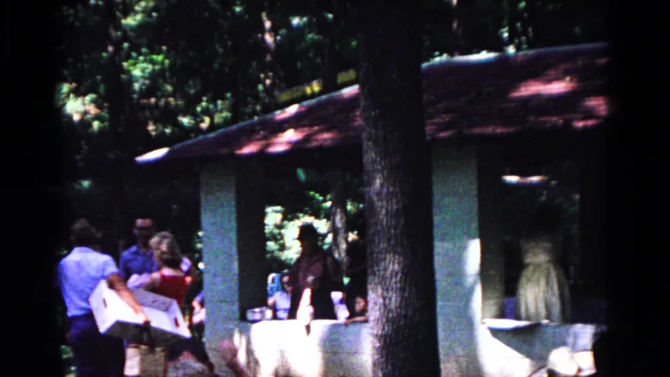 A man carries a large white item as adults gather near the pavilion in 1963 Cold Springs park footage.
