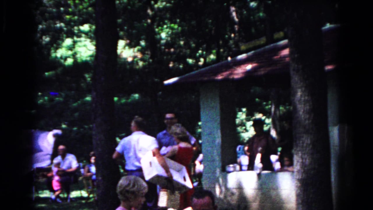 Adults mingle around a shaded pavilion in Cold Springs, New York, with picnic items visible in the 1963 footage.
