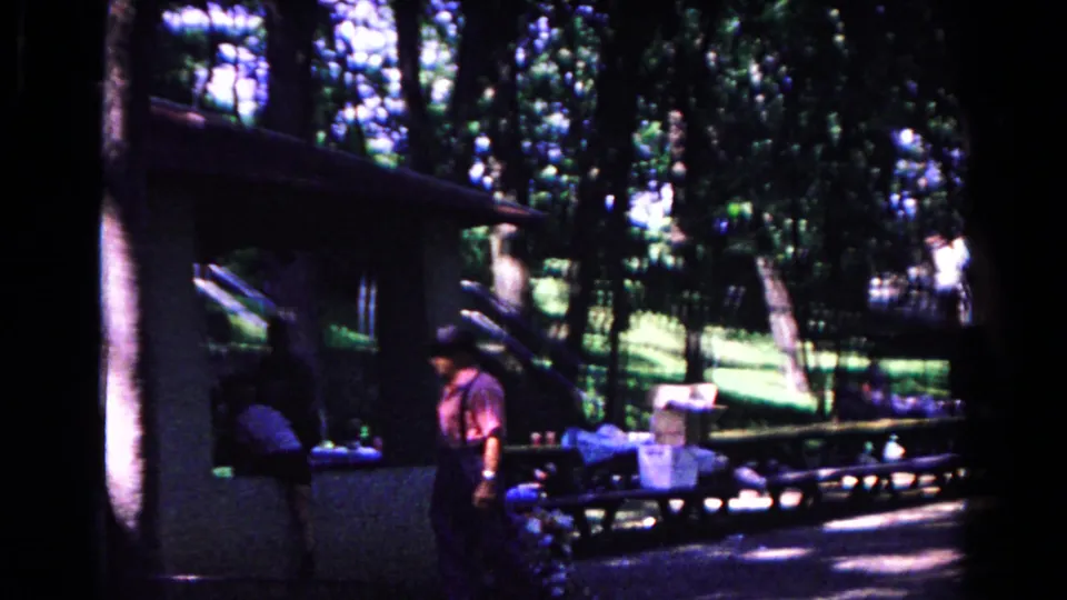 The scene shifts to a shaded picnic shelter area in the Cold Springs park, where a person stands near tables and packed items.