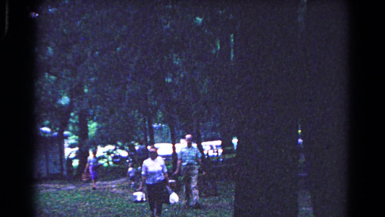 People walk through a shaded Cold Springs park in 1963, with picnic baskets and cars visible behind the trees.