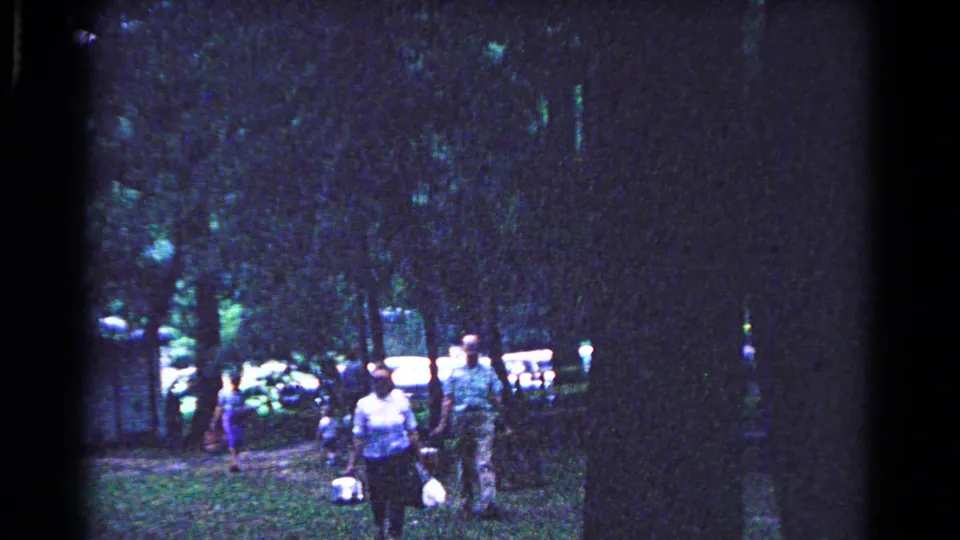 People walk through a shaded Cold Springs park in 1963, with picnic baskets and cars visible behind the trees.