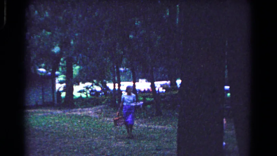 A final 1963 home-movie frame shows a woman moving through the shaded Cold Springs park as the picnic area recedes behind her.