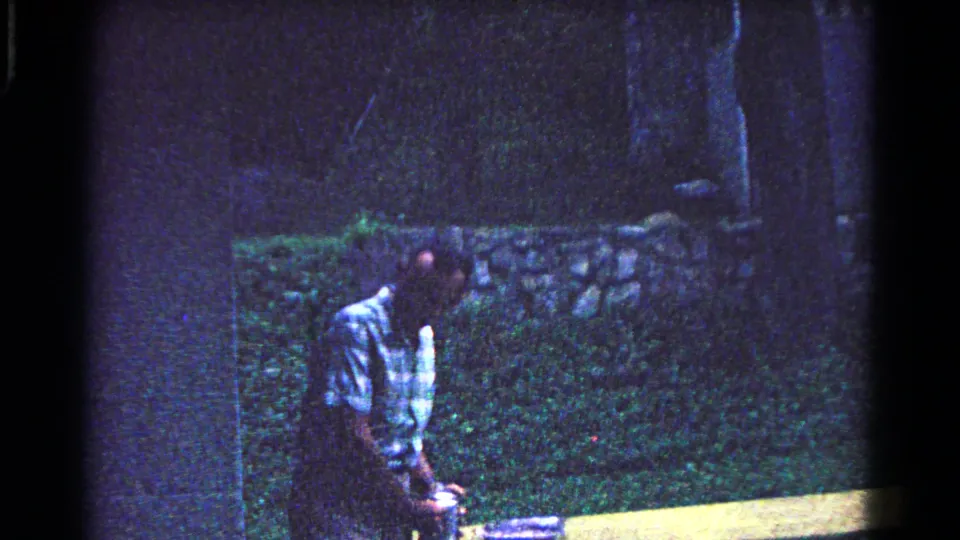 A man leans toward picnic items near a table in shaded 1963 Cold Springs, New York campground footage.