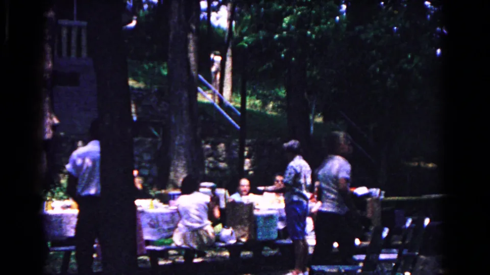 1963 Cold Springs picnic frame showing adults around tables with chairs, trees, and shaded ground.