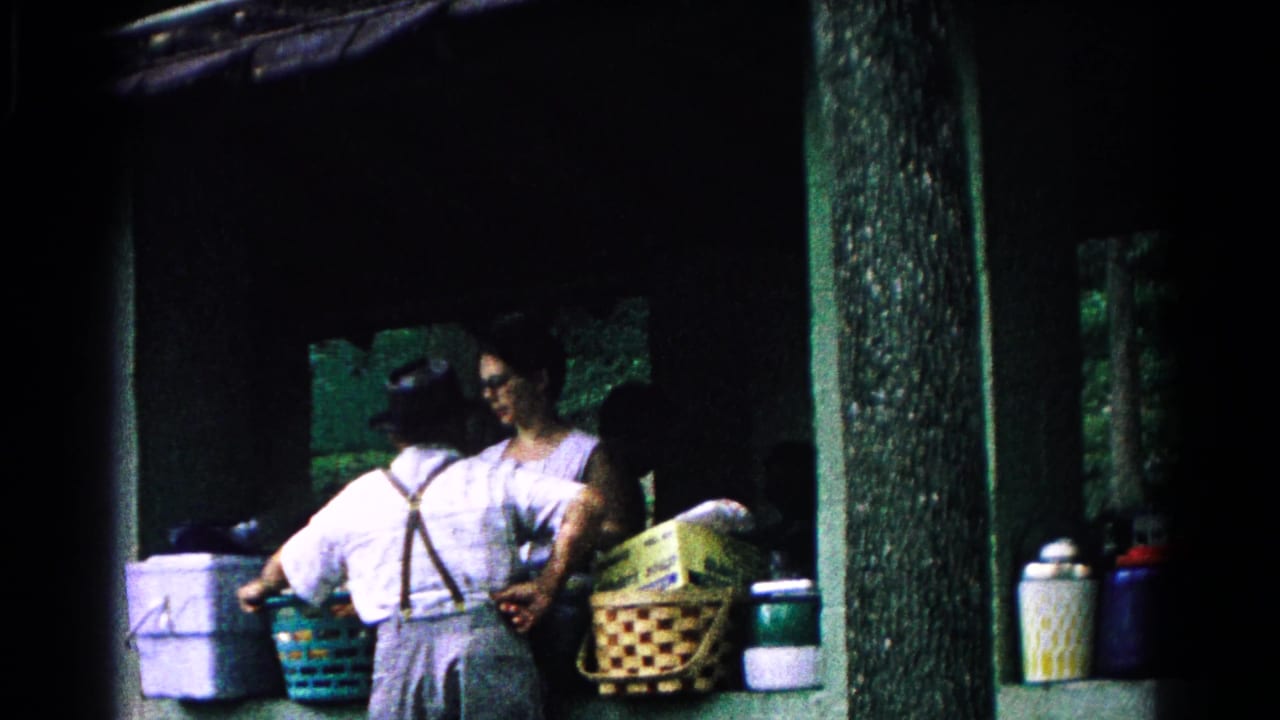 Adults under a shelter handle baskets and picnic supplies beside a table.