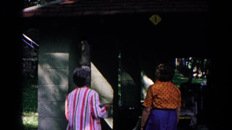 Two women are seen from behind near a small campground building in the wooded Cold Springs setting.