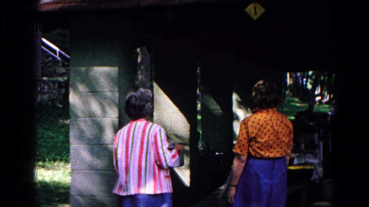 In 1963 Cold Springs, New York footage, two women stand beneath a covered outdoor food-service opening with stone supports and grass nearby.