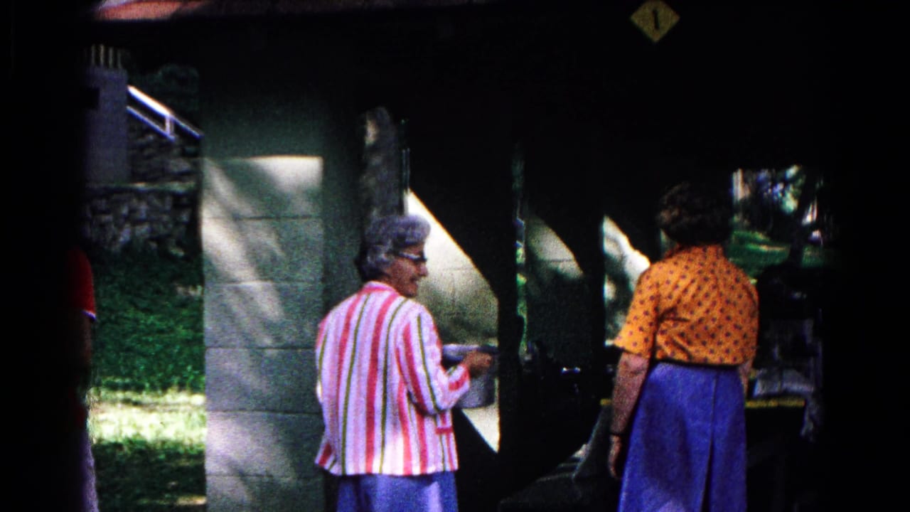 The women remain near the covered food-service window in Cold Springs, New York, with bright grass and stonework visible at the edge of shade.