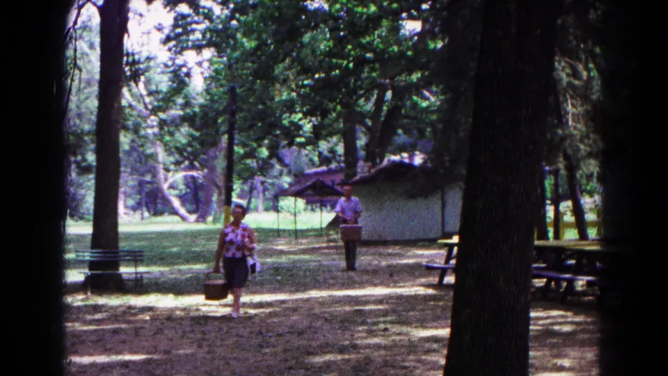 1963 Cold Springs, New York home-movie frame of two adults crossing a shaded picnic ground, with the woman nearer the camera.
