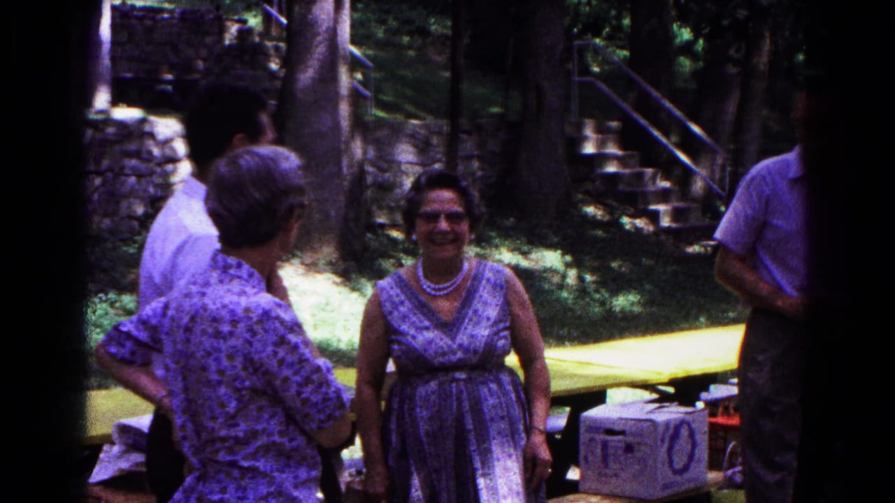 Adults gather near a yellow picnic table in a wooded park.