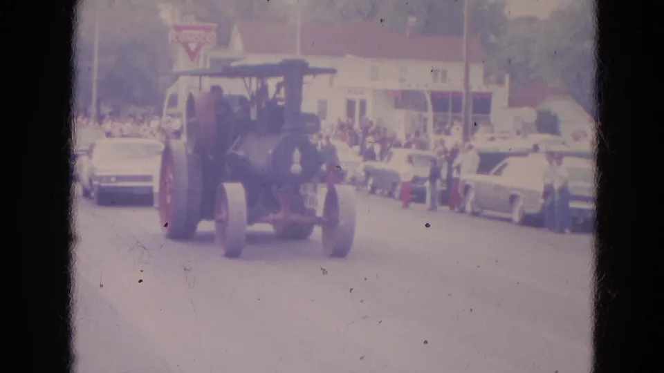 In Lincoln, Nebraska, 1963, a vintage steam tractor moves along a street parade route past spectators, classic cars, and a Conoco sign.