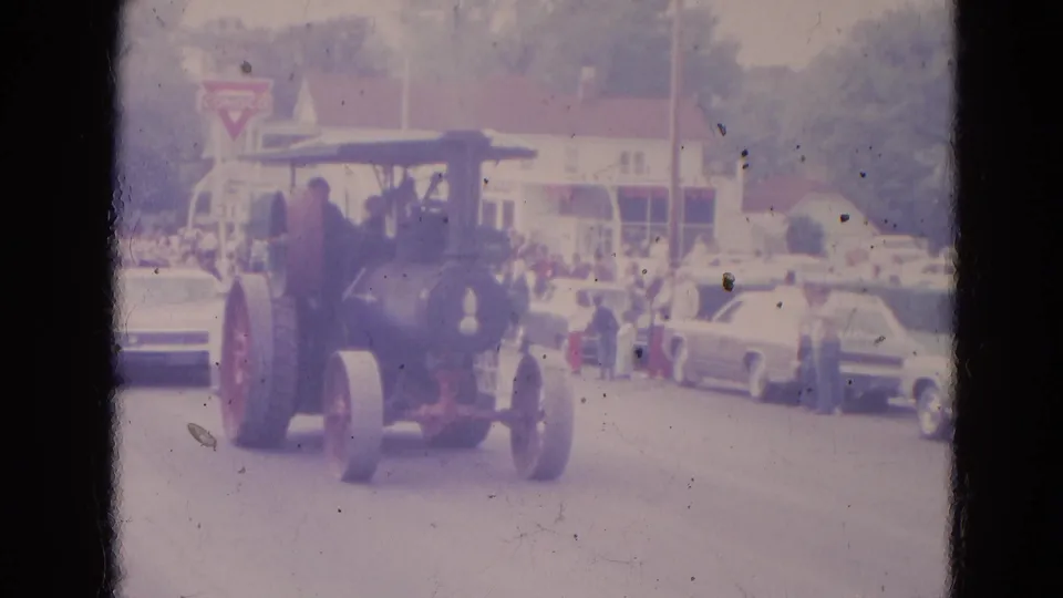 The vintage steam tractor is seen closer from the front on a Lincoln, Nebraska street, with spectators and early-1960s cars in the background.