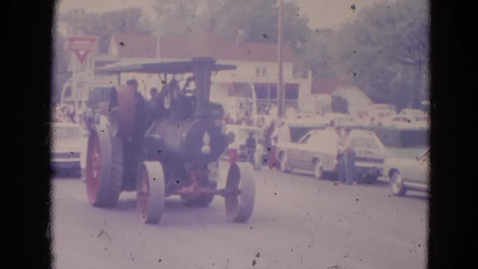 A 1963 Lincoln, Nebraska parade view shows the steam tractor passing classic cars, curbside spectators, low buildings, and a Conoco sign.