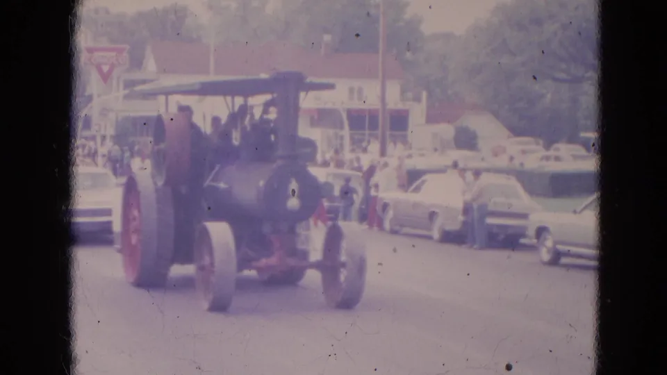 1963 Lincoln, Nebraska home-movie frame of a steam tractor moving down a street parade route with spectators and period cars nearby.