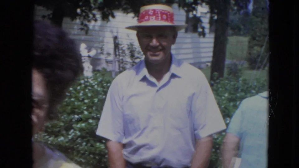 1963 Lincoln, Nebraska home-movie still of a man in a light shirt and red-banded hat standing in a garden.