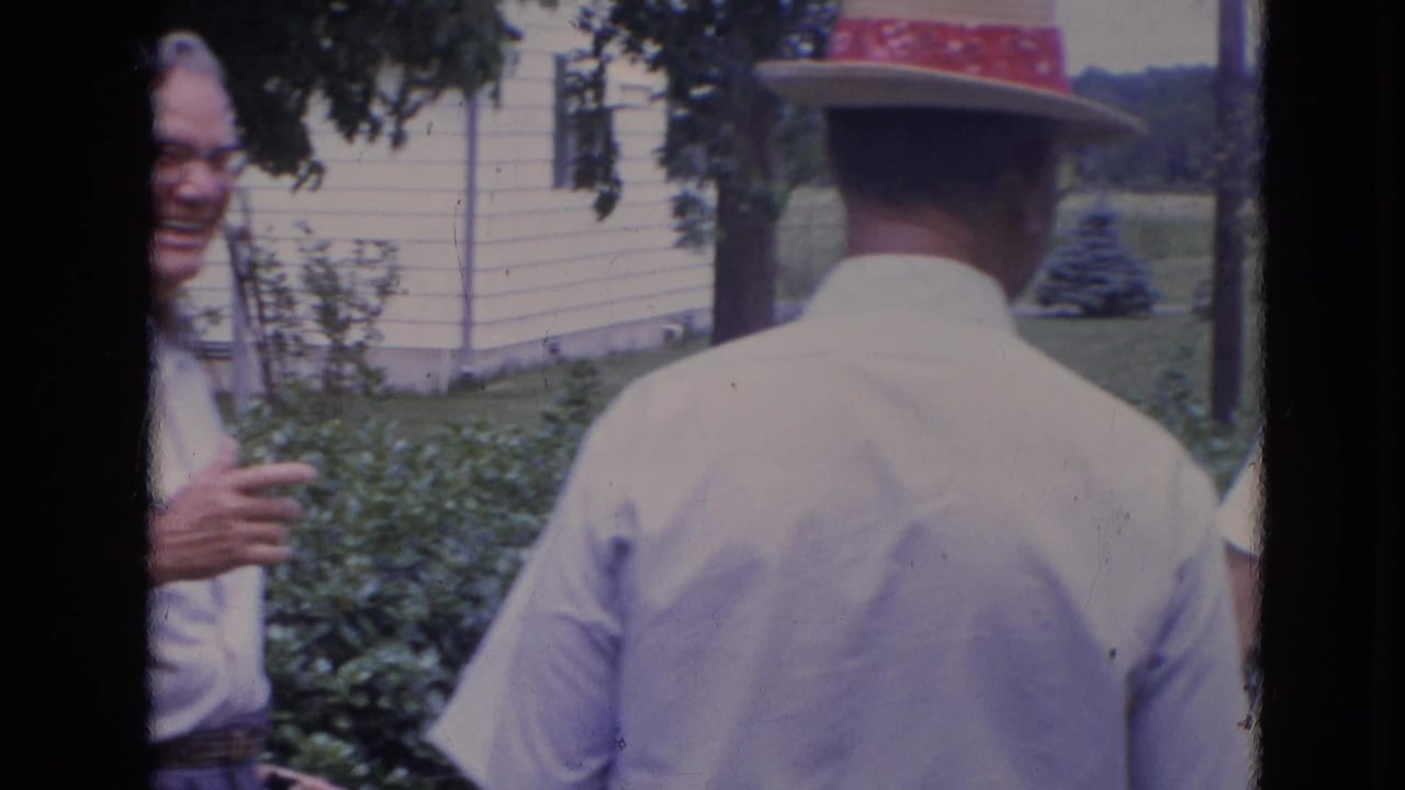Adults laughing in a backyard, with a man in a straw hat seen from behind.