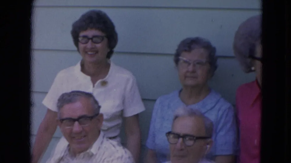 Five adults, including older relatives and a younger woman, pose together by house siding in Lincoln, Nebraska home-movie footage.