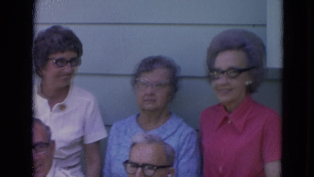 1963 Lincoln, Nebraska home-movie frame showing older adults in glasses gathered outdoors by light house siding.