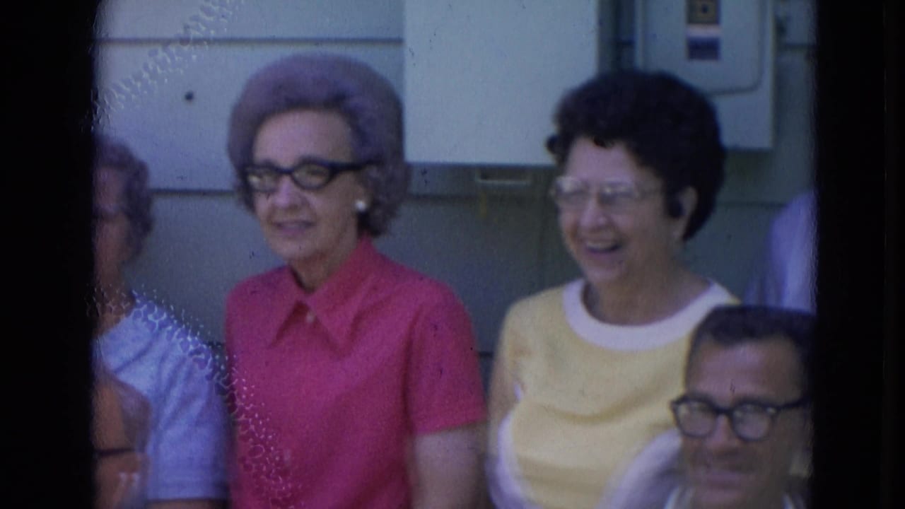 1963 Lincoln, Nebraska frame with smiling older women in pink and yellow tops beside seated men outdoors.