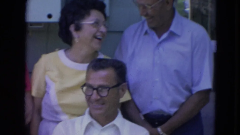 1963 Lincoln, Nebraska frame showing adults smiling and conversing outdoors during a casual gathering.