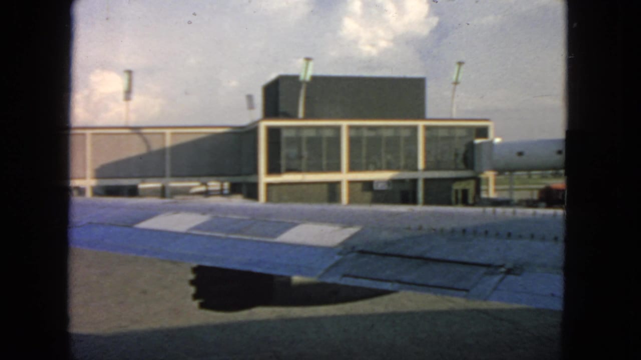 1963 San Francisco airport view from an airplane window, with a blue-and-white wing in front of a glass terminal.