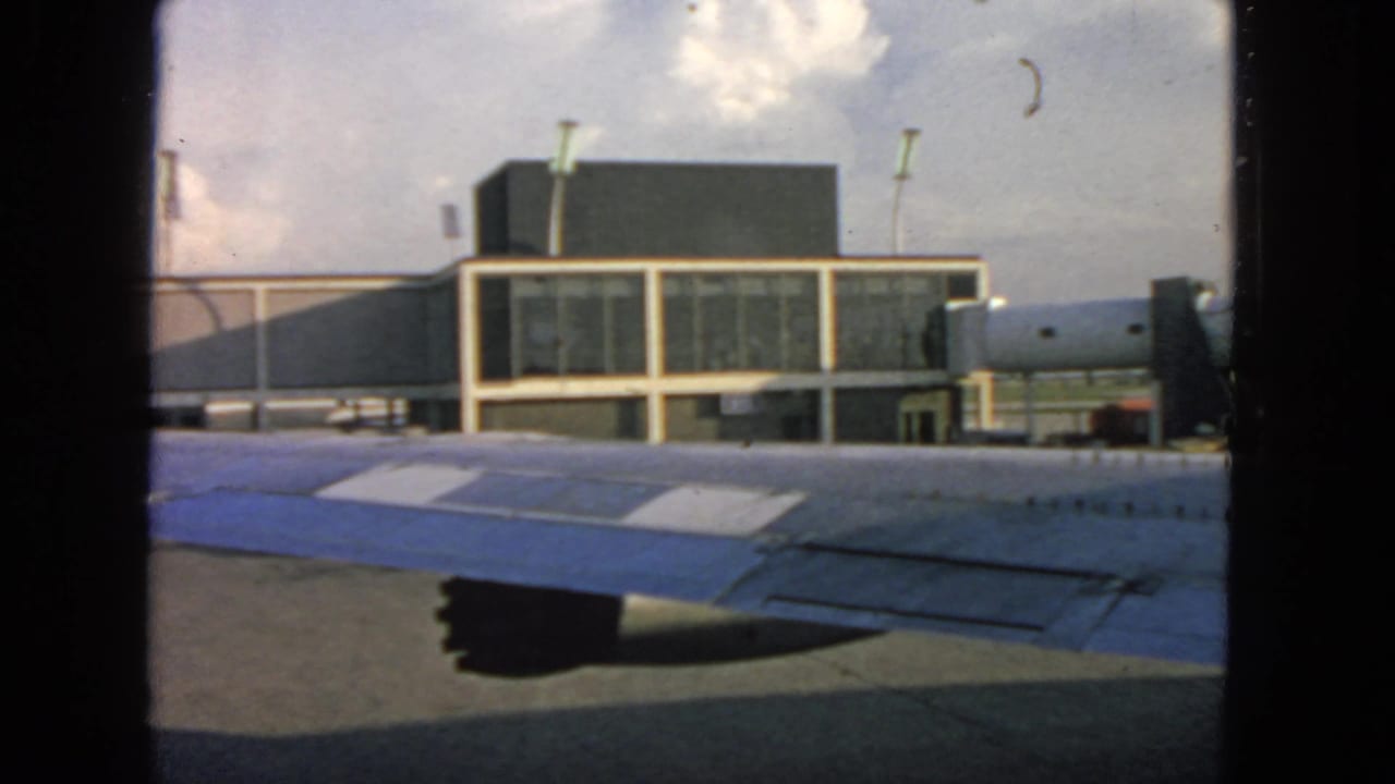 Airplane-window view at San Francisco in 1963, showing the wing, terminal facade, and tarmac structures.